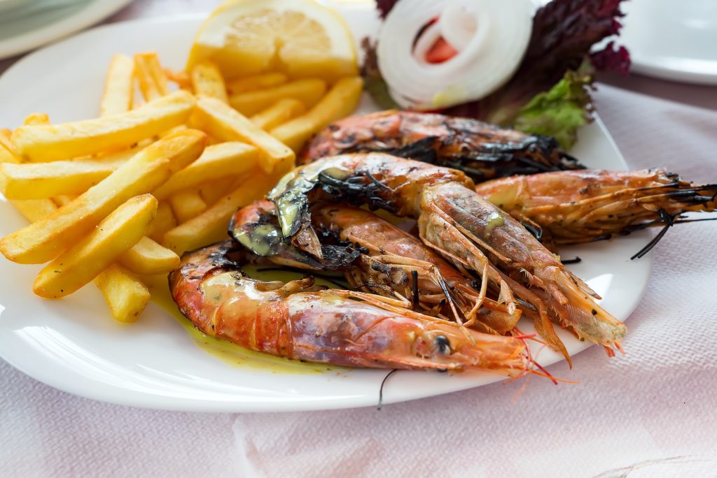 Close up big size grill shrimps with fried potato, vegetables and lemon, lunch time in restaurant